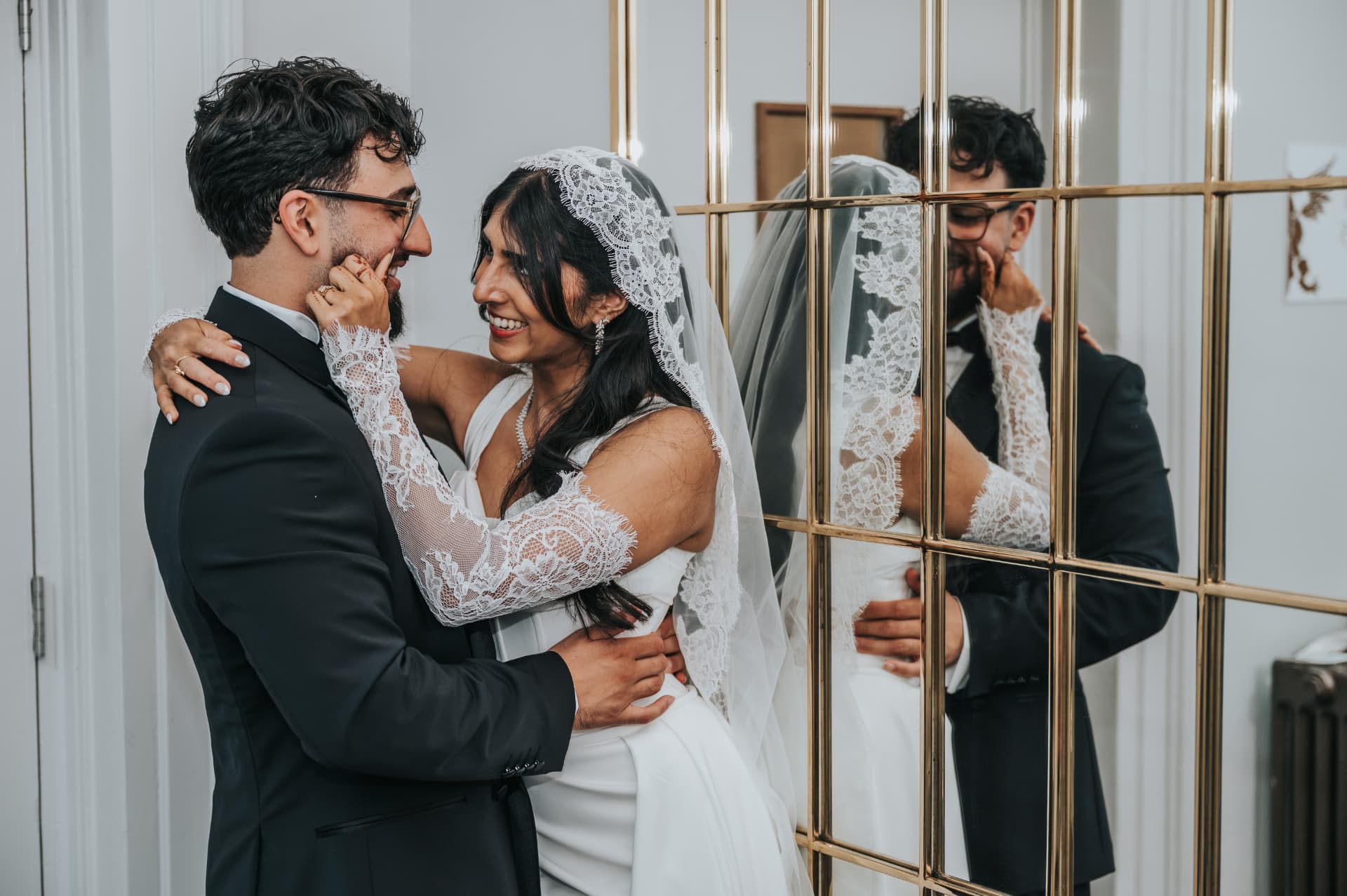 Bride and groom laughing together beside a gold-framed mirror