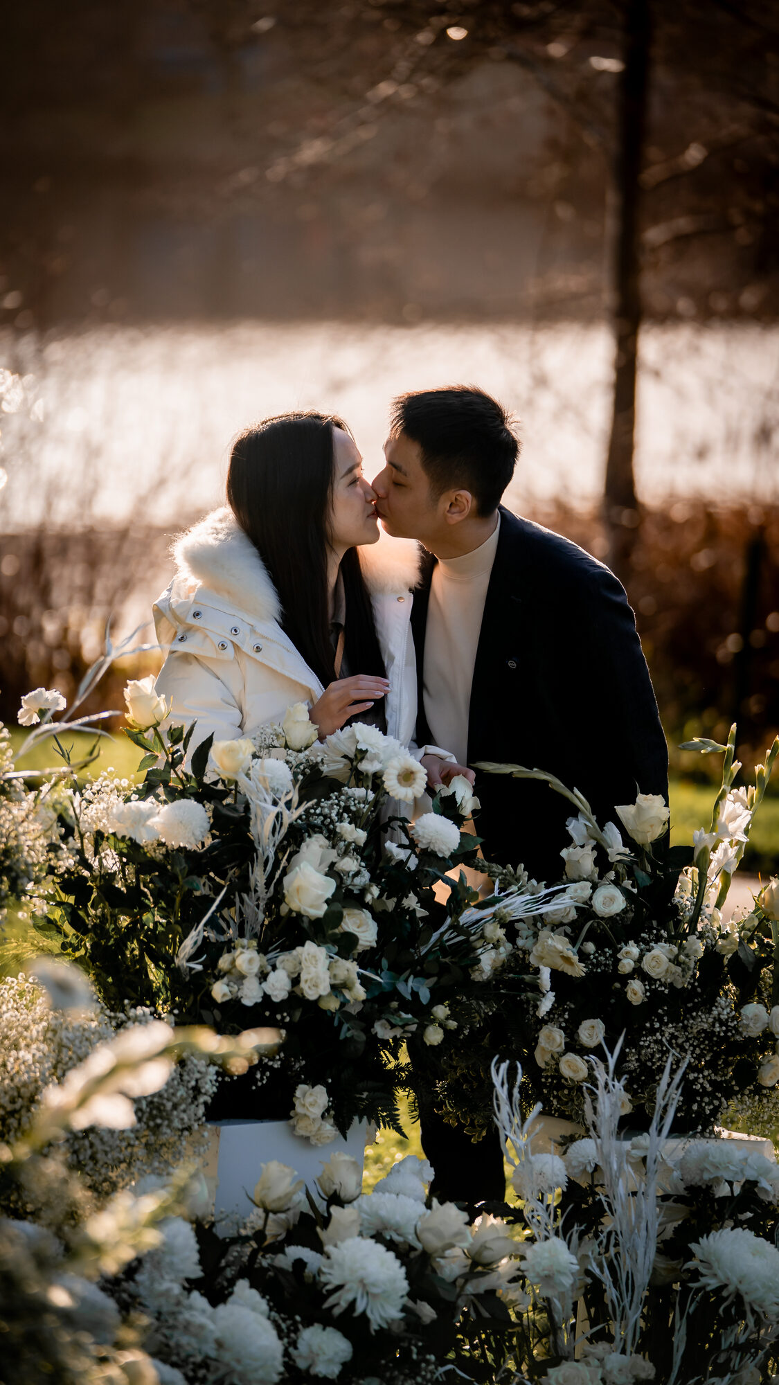 Couple kissing amongst a sea of white roses at sunset by the water