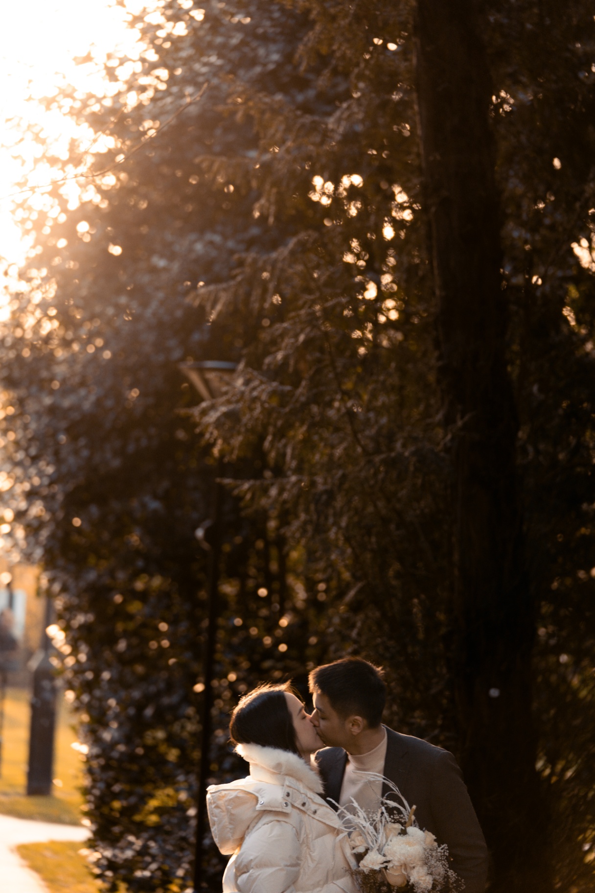 Couple kissing at sunset surrounded by sparkling bokeh and tall trees