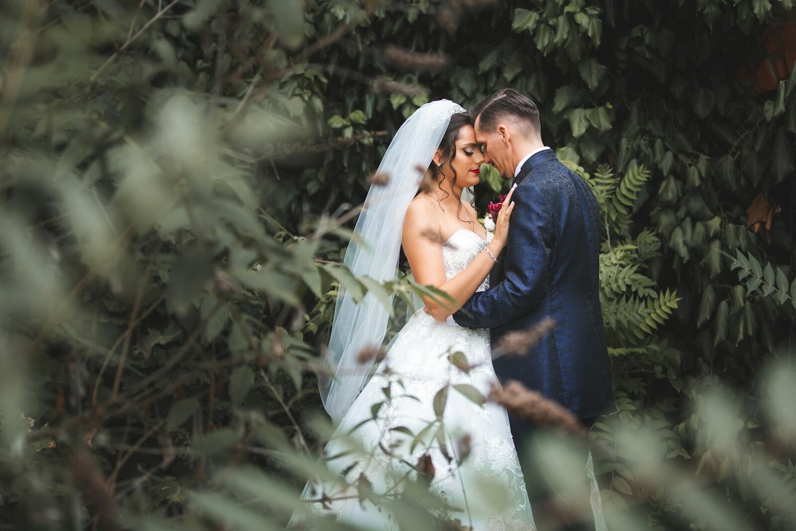 English bride and groom embracing in lush green foliage